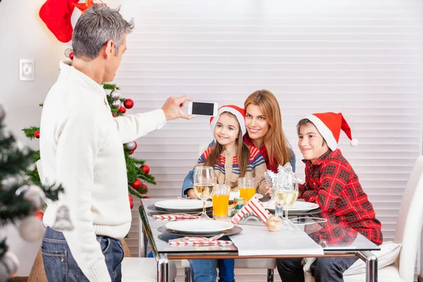 Семья за рождественским столом с отцом, фотографирующимся с детьми — стоковое фото