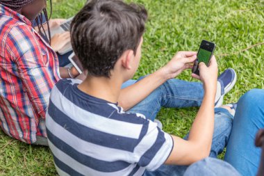 Çimenlerin üzerinde oturmuş akıllı telefonlar kullanan genç grup.