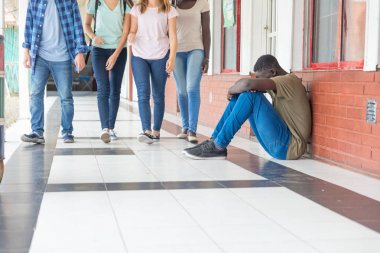 Zorbalık okul. Gençler yürüyüş ona karşı grup ise okul koridorunda oturmuş Afro Amerikalı erkek genç üzgün.