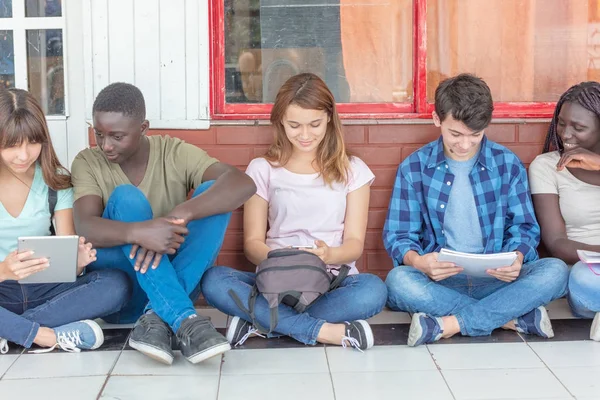 多民族的青少年使用电子阅读书籍坐在学校走廊 — 图库照片