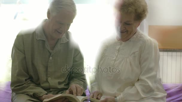高齢者男と女一緒にベッドの上に座って 本を読んでのカップル — ストック動画