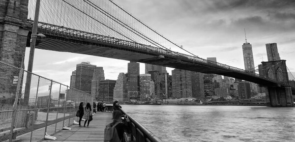 Black and white view of Brooklyn Bridge and Downtown Manhattan at sunset.