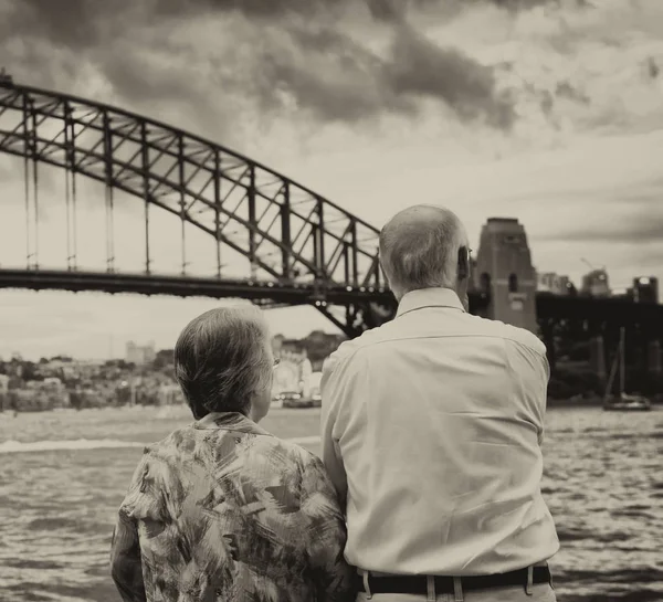 Elderly couple enjoy Sydney Harbour Bridge view at sunset.