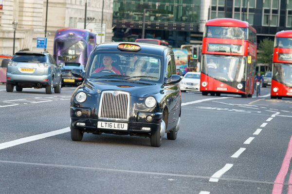 LONDON - SEPTEMBER 25, 2016: Red buses and black cab speed up in the streets. The city attracts 30 million tourists annually.