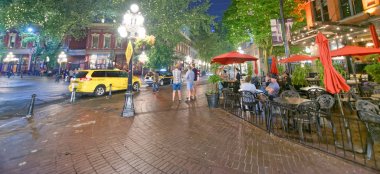 VANCOUVER, CANADA - AUGUST 8, 2017: Streets of Gastown with tourists at night. Vancouver attracts 10 million people annually. clipart