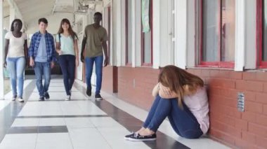 okul koridorda yürüyüş ve katta oturan ve ağlayan bir kız zorbalık genç grup