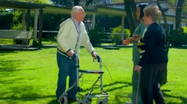 Yaşlı çift genç hemşire tarafından destekli bahçesinde gazete okuyor. Sağlık ve emeklilik kavramı