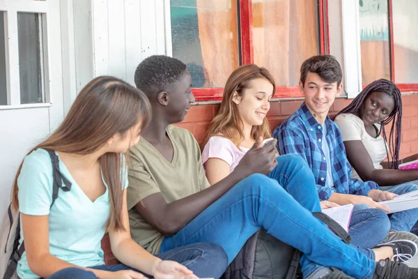 Grupa Nastolatków Mieszanej Rasy Rozmawiać Siedząc Korytarzu Szkoły — Zdjęcie stockowe