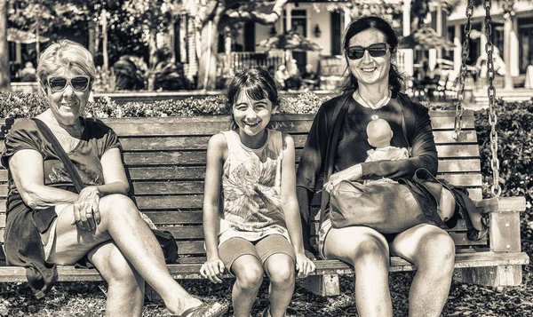 Three generations of women happy seated on a city bench.