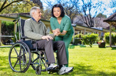 Asyalı doktor tekerlekli sandalyedeki yaşlı adama güvence veriyor..