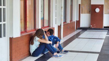 Genç Asyalı kız okulda üzgün bir şekilde yalnız oturuyor. Depresyondaki çocuk bir koridorda terk edildi ve tuğla duvara yaslandı. Zorbalık, ayrımcılık ve ırkçılık kavramı.
