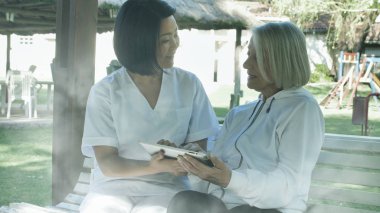 Asyalı doktor bahçede tablet kullanan yaşlı bir kadına yardım ediyor. Mutluluk ve emeklilik kavramı.