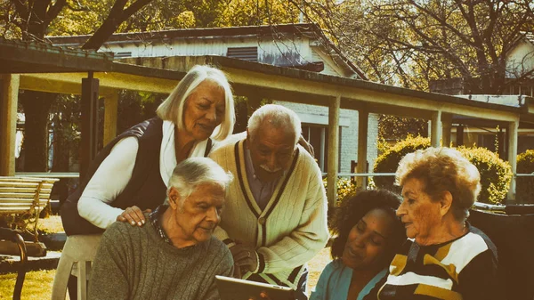 非洲护士带着两对老年退休夫妇在疗养院花园外面用平板电脑 康复和退休概念 — 图库照片