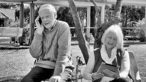 在阳光灿烂的日子里 一对快乐的退休夫妇在户外使用科技产品 — 图库照片