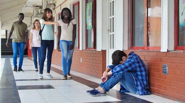 Young caucasian sitting alone with sad feeling at school. Child in depression abandoned in a corridor and leaning against brick wall. Bullying, discrimination and racism concept.