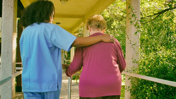 非洲女医生在医院院子里用手杖与年老的退休妇女交谈 康复和退休概念 — 图库照片