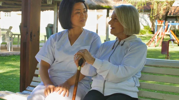 アジアの医師は 高齢者の退職女性にウォーカースティックで 両方の庭のベンチに座って話している 幸福と退職の概念 — ストック写真