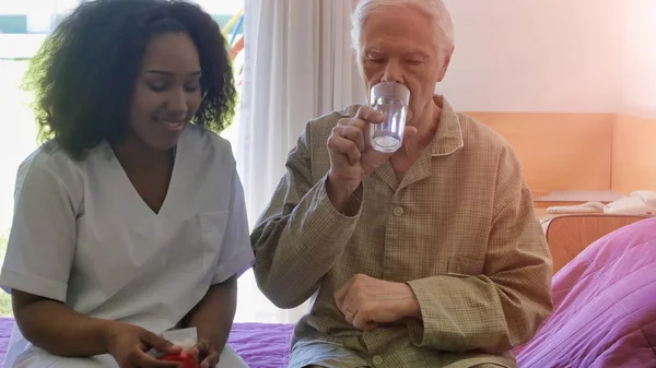 非洲女医生给躺在医院病床上的老年退休男子提供医疗药丸 康复和退休概念 — 图库照片