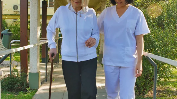病院の庭にウォーカーの棒で高齢者の女性を助けるアジアの医師 リハビリテーションの概念 — ストック写真