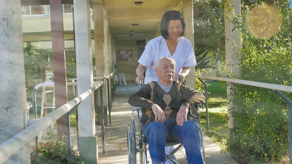 Asiatisk Kvinnlig Läkare Pratar Med Äldre Pensionerad Man Rullstolen Sjukhusgården Stockfoto