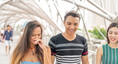 Üç Asyalı genç arkadaş şehirde yürüyor ve gülümsüyor.