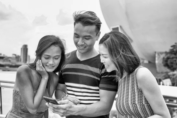 Três jovens amigos asiáticos revisando fotos da cidade no smartph — Fotografia de Stock