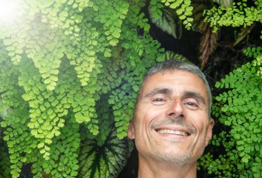 Yeşil bitki tarafından çerçevelenmiş mutlu adam. Doğa ve sürdürülebilirlik 