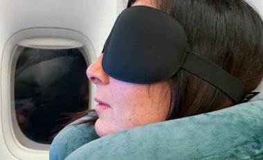 Protestoya giderken göz maskesi takan bir kadın uçak uçuşunda uyuyor.