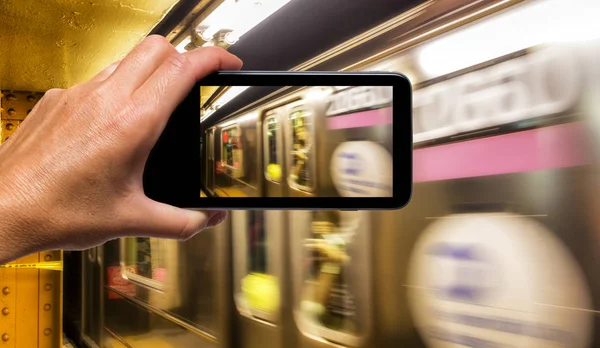 Female hand with smartphone taking a picture of New York subway train. Tourism concept.