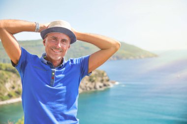 Hasır şapkalı adam denizde dinleniyor, arkada okyanus var..