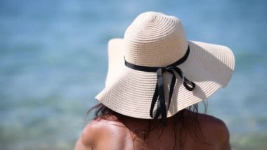 Bikini ve hasır şapkalı bir kadının tropik plajda güneşlenişini gösteren arka plan görüntüleri.