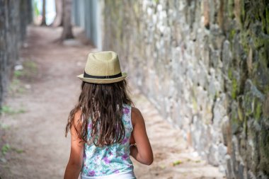 Dar bir sokakta hasır şapka takarak yürüyen genç bir kız. Macera konsepti.