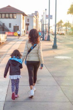 Kızıyla birlikte okyanus kıyısında yürüyen bir kadın..