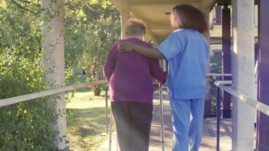 Kıdemli kadın hemşiresinin yardımıyla yürüyor.