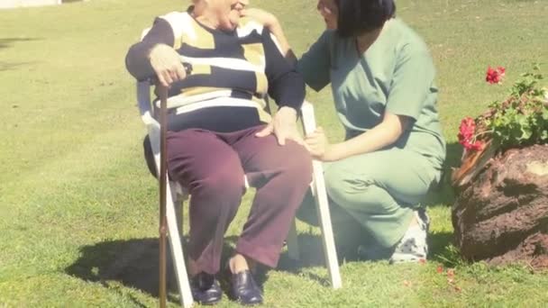 Enfermera asiática sonriendo al aire libre con anciana con muletas, la luz del sol que viene de arriba — Vídeos de Stock