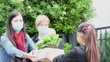 Coronavirus acil durumu için maskeli iki kadına çiçek veren genç bir kız.