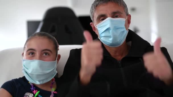 Webcam vista de la niña con el padre durante un videocall con su madre en caso de emergencia coronavirus, ambos con máscaras. Tiempo en familia, concepto de actividad divertida — Vídeos de Stock