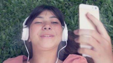 Mutlu Asyalı kız çimlere uzanıp müzik dinliyor ve şarkı söylüyor.