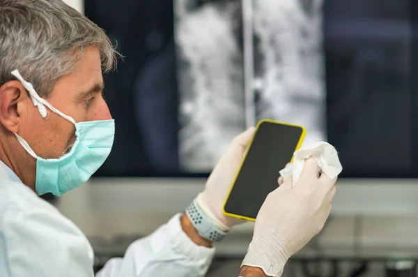 Muž Doktor Své Kanceláři Masce Čistí Svůj Smartphone — Stock fotografie