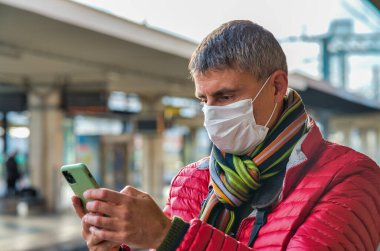 Coronavirus salgınında akıllı telefon tutan maskeli bir adam..