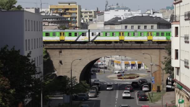 Varsovia Puente de cruce de trenes en la ciudad. La vida depende de un día de la semana con el paso elevado del metro. Muchos coches y viajeros. Actividades humanas en las calles de Varsovia. Tren verde pasa a través de un cruce ferroviario, entre las casas — Vídeos de Stock