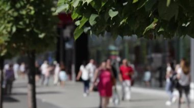 Sokakta insanlar yürüyüş kalabalık. Yaz güneşli gün, insanlar sokakta yazlık giysiler giymiş. Ön planda, ağaçlar yeşil. İnsanlar sokakta yürürken. Kız bikini, şehir salonu sergilenen arıyorum. Konuşan iki iş kadınları bir