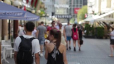 İnsanlar sokakta yürürken. Sokakta insanlar yürüyüş kalabalık. Yaz güneşli gün, insanlar sokakta yazlık giysiler giymiş. Ön plan, yeşil ağaçlar içinde odak içinde değil. İnsanlar sokakta yürürken. Varşova 06.02.2015