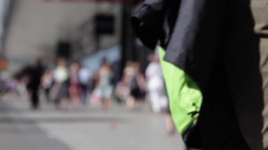 İnsanlar sokakta yürürken. Sokakta insanlar yürüyüş kalabalık. Yaz güneşli gün, insanlar sokakta yazlık giysiler giymiş. Ön plan, yeşil ağaçlar içinde odak içinde değil. İnsanlar sokakta yürürken.