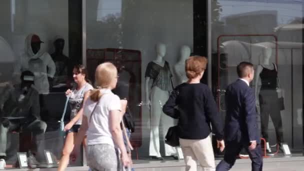 Skara människor promenad på gatan. Solig sommardag, människor på gatan klädd i sommarkläder. I förgrunden, gröna träden. Människor går ner på gatan. Flickvänner tittar på bikini på butikdisplay i staden. Två affärskvinnorna talar ett — Stockvideo