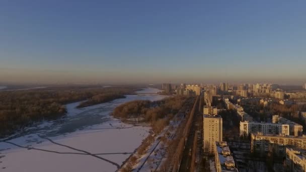 Киев. Украина. Мост через реку Днепр Зима. Пролетим над городом с высоты птичьего полета на закат Лонза. Город Киев находится на Днепре. Летают в Киеве по Днепру на закате. Крыши многоквартирных домов — стоковое видео