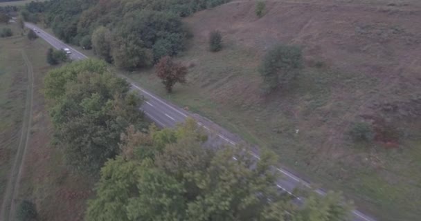 Luftaufnahme. Autobahn in der Nähe des Berges Straße mit Blick auf Autos von oben. grüne Bäume am Straßenrand. Sommerbedeckter Tag. ein Feld mit einem kleinen Fluss in der Nähe der Straße. Autos fahren über die Autobahn. — Stockvideo