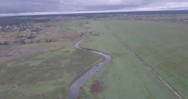 Inspección aérea. un pequeño río pasa a través de un campo verde. Un hermoso campo con vista al río desde la vista de un pájaro. día de verano, las sombras de las nubes yacen en el campo . — Vídeo de stock