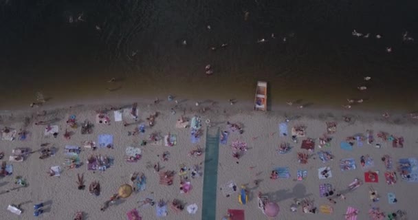 Antena z plaży. słoneczny letni dzień, ludzie są opalając się na żółtym piszczenie na brzegu Dniepru rzeki Kijowa. dzień wolny, wakacje na plaży. duża liczba turystów pływać. — Wideo stockowe