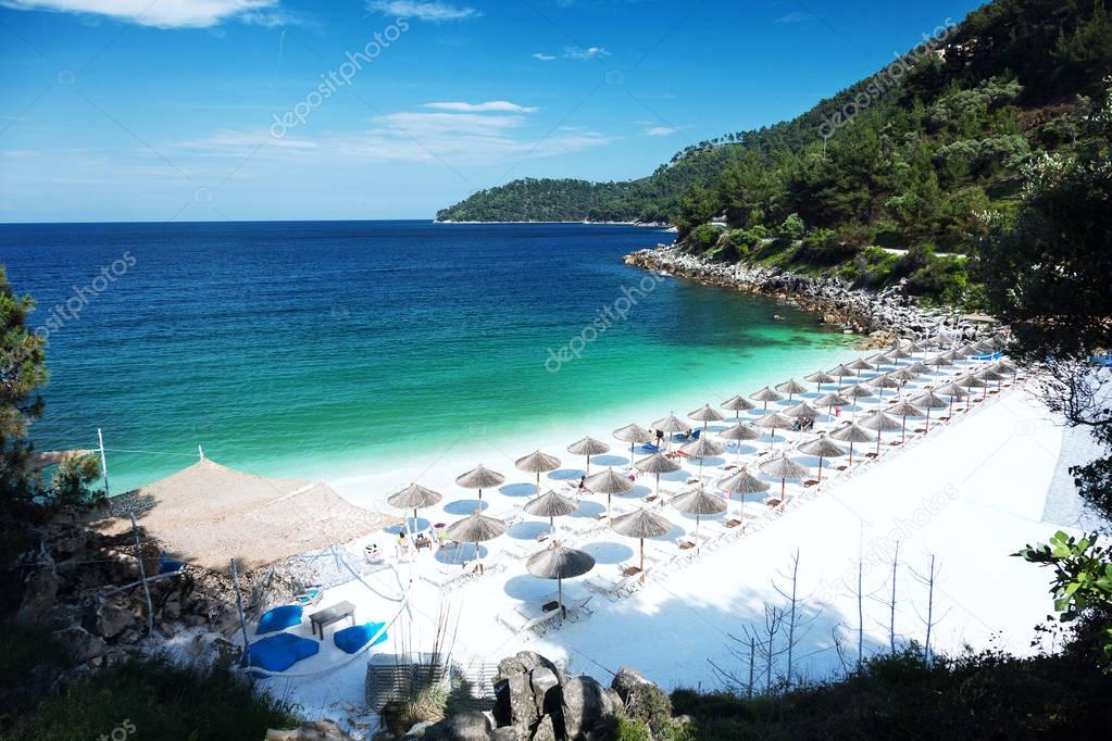 Marble beach (Saliara beach), Thassos Islands, Greece. Straw umbrellas (straw parasols) and sunbeds on the beach.
